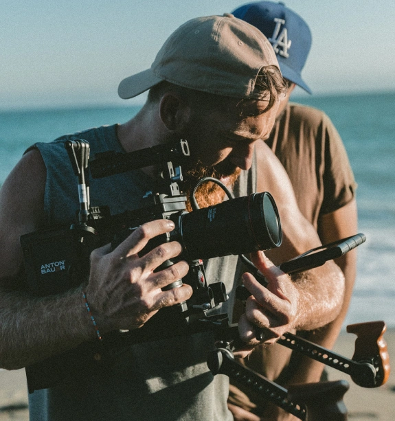 Two videographers filming at the beach with professional camera equipment.