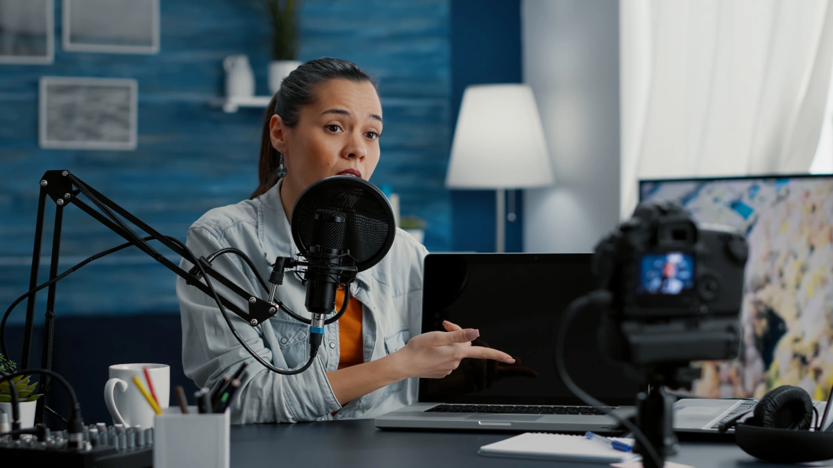 A woman seated at a desk, focused on her laptop, with a microphone positioned in front of her for clear audio.