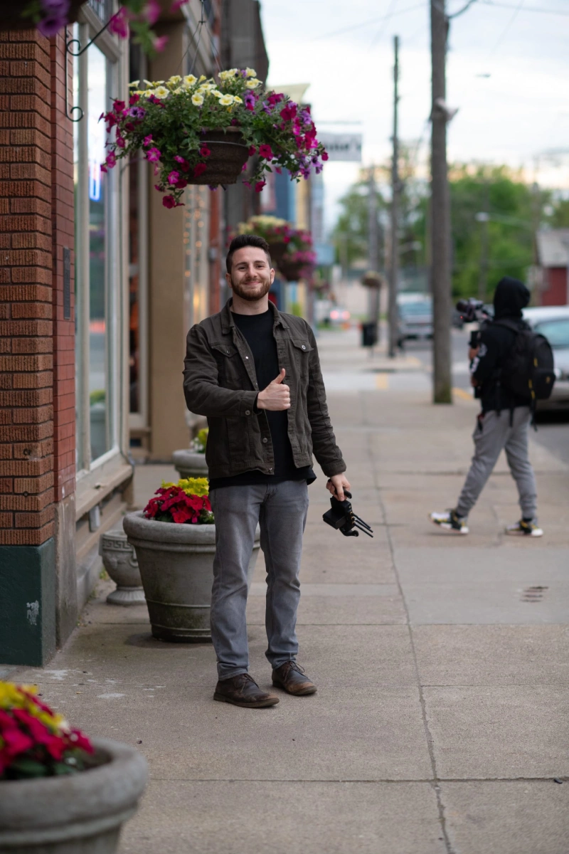 A man stands on a sidewalk, holding a camera, ready to capture the surrounding scenery.