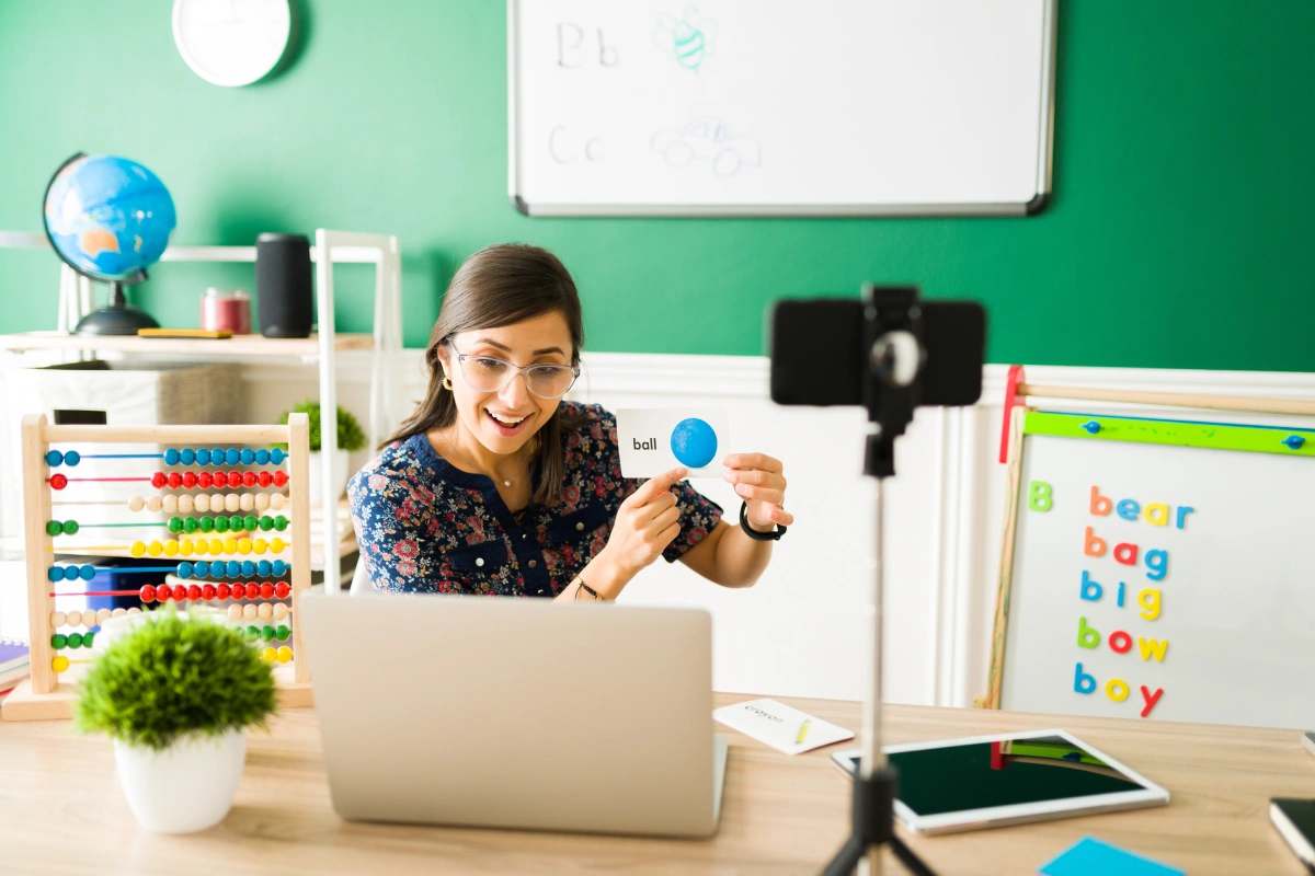 A woman seated at a desk, working on a laptop with a camera positioned nearby, focused on her tasks.